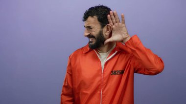 Sakallı, hapishane tulumu giymiş İspanyol bir adam mor arka plandan dinliyordu..