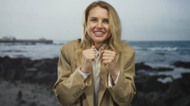 Sahilde mutlu bir şekilde gülümseyen bir kadın. Arka planda okyanus dalgaları ve kayalar var. Açık deniz manzarası arasında neşe ve özgürlüğü ifade ediyor..