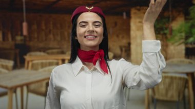 Üniformalı İspanyol kadın uçuş görevlisi, ahşap mobilyalarla dolu bir restoranda terasta eğlenirken öpücük yolluyor..