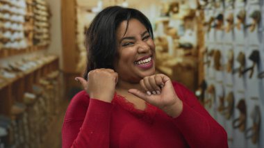 Perakende mağazasında gülümseyen kırmızı bir kazak giyen ve arka planda giysileri olan bir kadın, kapalı bir dükkan ortamında mutlu bir alışveriş deneyimi yaşadığını gösteriyor..