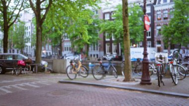Amsterdam 'da bir kanal boyunca park halindeki bisikletlerin bulanık manzarası, arka planda ağaçlar ve geleneksel mimari ile Avrupa' nın rahat bir kentinin özünü yakalıyor..
