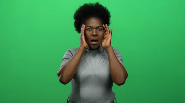 Gözü açık ve elleri yeşil arka planda olan, gri süveter giyen, canlı stüdyo çekimlerinde duygularını ve ifadesini ifade eden bir kadın şaşkınlığını ifade ediyor..