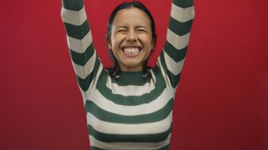 İzole edilmiş kırmızı arka planda televizyon kumandası olan İspanyol genç bir kadın heyecan ve coşku dolu bir jest yapıyor..