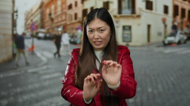Kırmızı ceketli bir kadın şehir sokaklarında hareketsiz duruyor. Geçmişi bulanık, hayat dolu ve yürüyen insanlar var..