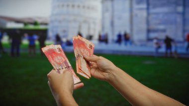 Pisa 'nın ünlü kulesinin yakınındaki bir şehir sokağında Güney Afrika rand' ını elinde tutan adam, canlı bir şehir ortamında iş ve para değişimi sergiliyor..