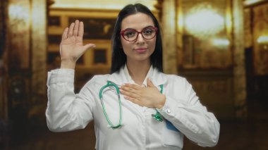 Beyaz önlüklü, steteskoplu bir kadın kilisenin iç kısmında duruyor, el göğsünde yemin işareti var, kırmızı gözlüklü, kutsal ortamda profesyonel görünümü arttırıyor.