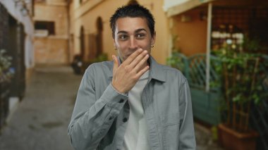 Yaşlı bir kasabanın dış mekanında ağzını kapayan genç bir İspanyol adam, bulanık bir tarihi mimariye karşı şaşkınlık sergiliyor..