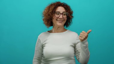 Gülümseyen, esmer, orta yaşlı, gözlüklü, soyutlanmış, mavi arkaplan, sıradan tarz, baş parmaklar yukarı, mutluluk, pozitif ifade.