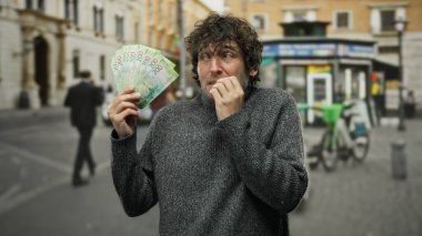 Çivi yiyen İspanyol bir adam şehir sokaklarında endişeyle Rus rublesini tutuyor. Mali güvensizliği ve dışarıdaki endişeyi yansıtıyor..