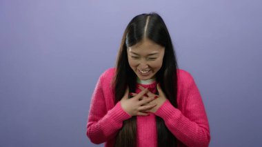 Mor arka planda pembe süveter giyen, el hareketleriyle gülümseyen, neşe ve ifadeyi somutlaştıran bir kadın..