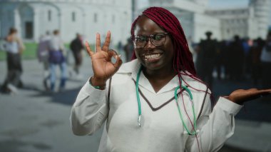 Steteskop hareketleriyle Afro-Amerikalı kadın tamam ve kalabalık bir şehir caddesinde elini gösteriyor..