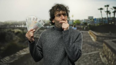 Czech Koruna banknotlarını elinde tutan İspanyol bir adam şehir sokaklarında düşünceli bir şekilde para biriktiriyor..