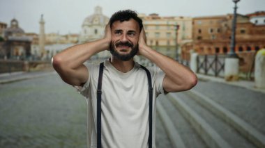 Eski Roma 'da sakallı, sıkıntılı görünen İspanyol bir adam. Tarihi mimarinin yumuşak odaklı arka planına karşı pantolon askısı takıyor.