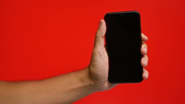 Akıllı telefonu olan adam canlı kırmızı arka planda modern teknoloji ve iletişim gereksinimlerini vurguluyor.