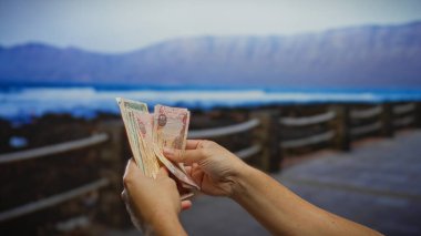 Deniz kenarındaki kirli paraları tutan eller. Sahilde manzaralı bir arka planda para sayan bir adamı tasvir ediyor. İşletme ve döviz kurunu vurguluyor..