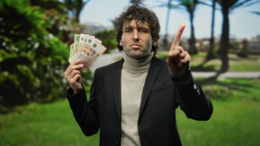 Parktaki İspanyol adam bir parmağını uzatmış Arjantin pesolarını tutuyor. Çevresi yemyeşil, açık havada bir iş ya da finans teması yakalıyor..