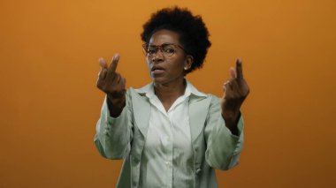 İki orta parmağı izole edilmiş turuncu arka planda kaldırılmış kaba bir jest yapan bir kadın, profesyonel bir kıyafetle yoğun bir yüz ifadesi ile hayal kırıklığını ve meydan okumayı ifade ediyor..