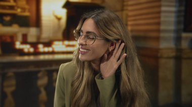 Tarihi kilisede gözlük takan iş kadını kulağına hürmet gösterme özverisini yansıtıyor..