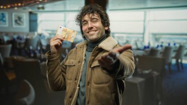 Avro banknotunu tutan gülümseyen bir adam rahat bir restoran ortamında elini uzatıyor. Hafif ışıklandırma dostça bir değiş tokuş anını ve sıcaklığı yakalıyor..