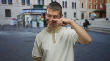 Gülümseyen adam, sokak ortasında şehir geçmişine karşı günlük gömleğiyle burnunu işaret ediyor..