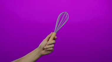 Canlı pembe arka plana karşı çırpı tutan bir adam günlük mutfak gereçlerinin zıt unsurlarını ve renkli ayarları vurguluyor..