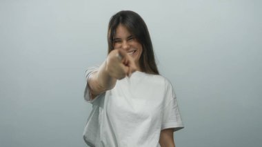 Beyaz arka planda gülümseyen ve kameraya işaret eden bir kadın kapalı bir stüdyoda günlük giysiler giyerek mutluluk ve güven saçar..