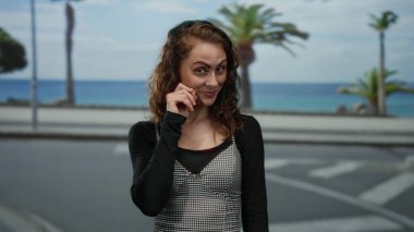 Deniz manzaralı güneşli gezinti yaparken neşeli bir şekilde gülümseyen kadın, arka planda palmiye ağaçları ile deniz kenarındaki bağlamda gençlik ifadesini sergiliyor.