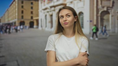 Yoğun bir şehir caddesinde, günlük giysiler içinde, şehir hayatı ve mimarisi tarafından çevrelenmiş bir merak ve güven ifadesiyle duran bir kadın günlük anları yakalıyor..