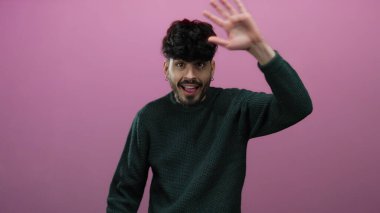 Pembe arka planda jest yapan genç adam yeşil süveter giyiyor canlı bir ifade ve tarz sergiliyor.