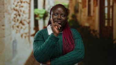 Şehir caddesinde açık havada duran bir kadın düşünceli bir ifade ve örgü örerek kentsel çevreyi gösteren binalarla çevrili bir şeyi sorguluyor.