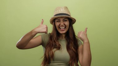 Uzun saçlı ve şapkalı gülümseyen kadın sarı arka planda başparmak kaldırıyor. Rahatlamış bir şekilde mutluluk ve pozitifliği ifade ediyor..