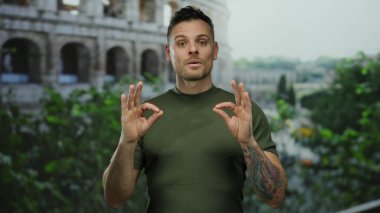 Roma Kolezyumu 'nun yakınında meditasyon yapan genç bir adam, sakin bir ifade sergiliyor, arka planda yemyeşil bir ortam var, kentsel bir ortamda sükunet öneriyor..