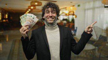 Otel resepsiyonunda elinde Arjantin pezosu olan İspanyol bir adam kendinden emin bir gülümseme ile bir tarafı işaret ederek, kapalı bir ortamda finansal başarıyı resmediyor..