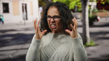 Şehir sokaklarında duygularını ifade eden kıvırcık saçlı, süveter ve gözlük takan şehir ortamında hayal kırıklığını bulanık arka planda canlandıran bir kadın..