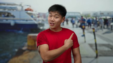 Deniz kıyısındaki limanda tekneli kırmızı tişörtlü genç Çinli adam ve açık havada canlı bir sahne yaratanlar..
