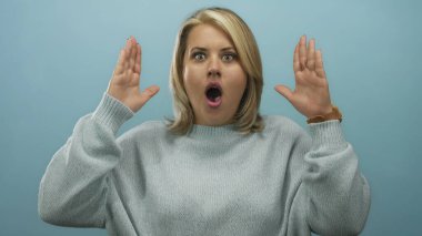 Genç sarışın kadın avuçlarını açık mavi stüdyo duvarına doğru kaldırıyor..