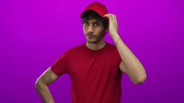 Kırmızı gömlekli adam kırmızı başlığı bir eliyle düzeltir ve diğerini mor arka planlı stüdyoya yerleştirir; kararlılık.