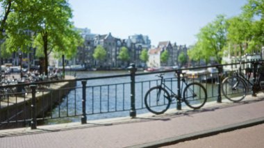 Odaklanamayan bisiklet ve köprüyle Amsterdam Kanalı 'nın bulanık görüntüsü, baharda yeşil ağaçlar ve Hollanda mimarisinin arka planı.
