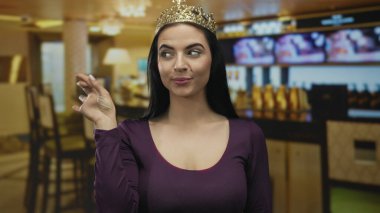 Taçlı İspanyol kadın, sıcak ışıklandırmalı, kapalı bir restoranda zarafet ve iletişim sağlayan bir kafede ağzını kapatarak el kol hareketi yapıyor..