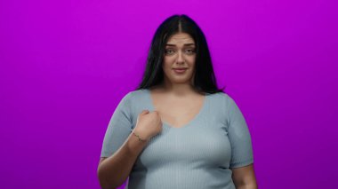 Genç bir kadın, kendine canlı pembe arka planda işaret ederken, kendine güveni olan bir gülümsemeyle anlaşmazlığını dile getirirken el kol hareketi yapar..