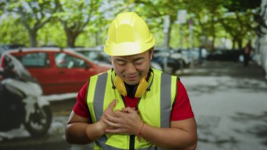 Kasklı gülümseyen adam güneşli bir günde arka planda arabaları olan kalabalık bir şehir sokağında şükranlarını sunuyor.
