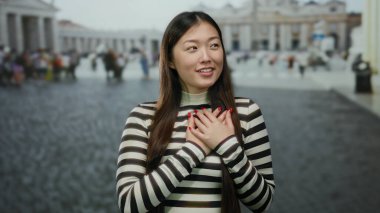 Vatikan 'da elleri göğsünde, çizgili bir bluz giymiş, geçmişi bulanık ve kaldırım taşı sokağında Aziz Peter Meydanı' nda gülümseyen bir kadın..