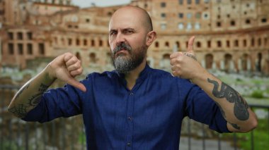 Sakallı ve dövmeli bir adam Roma harabelerinin önünde dikilip karışık fikirler beyan ediyor..