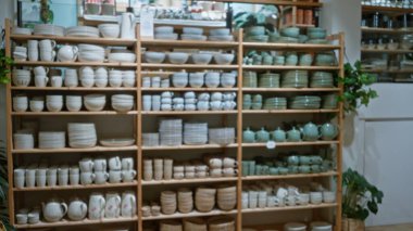 Dekor dükkanında raflar dolusu seramik kaseler ve tabaklar olan bir vitrin, bulanık bir arka plan ve yumuşak bokeh ile çekilen kapalı mekanda estetik bir bozulma yaratıyor..