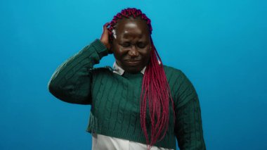 Mavi arka planda yeşil süveter giyen pembe örgülü kadın izole edilmiş portre ortamında düşünceli ve düşünceli görünüyor..