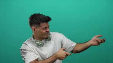 Kulaklıklı genç adam canlı yeşil arka plana karşı ip çekiyormuş gibi yapıyor. Şatafatlı hareketler ve modern stili gösteriyor.