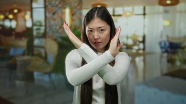 Şık bir otel ortamında kollarını kavuşturup el kol hareketi yapan bir kadın net bir ifade ve canlı bir ortam sergiliyor..