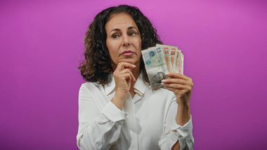 Soyutlanmış mor bir geçmişe karşı elinde İngiliz sterlinli banknotlar tutan orta yaşlı bir kadın, finansal değerlendirmeyi öneriyor..