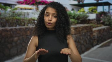 Genç İspanyol kadın taştan duvarın yanında açık avuçlar ve gün ışığında çiçek açan çalılar gösteriyor..