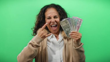 Orta yaşlı bir kadın, yeşil bir zemine karşı Hint banknotlarıyla poz veriyor. Güvenini ve finansal gücünü gösteren bir jest yapıyor..